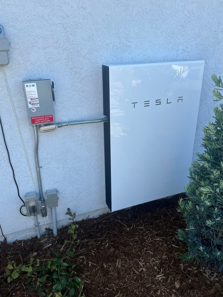 Tesla Powerwall mounted on an exterior stucco wall beside a PV disconnect
