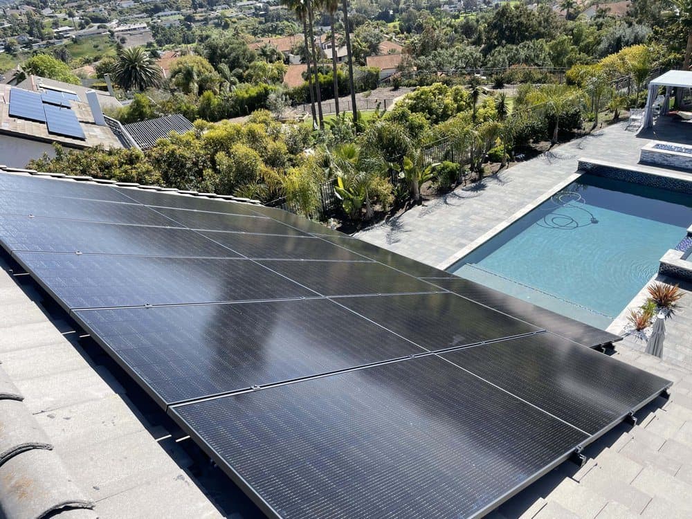 Aerial view of a black solar array on a low-slope roof beside a backyard pool