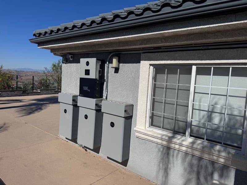 Three wall-mounted battery units and an inverter on the exterior of a stucco home